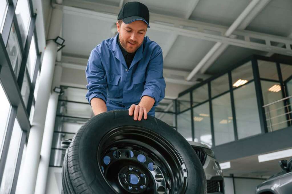 Front view, moving the tire. Man in blue uniform is working in the car service.