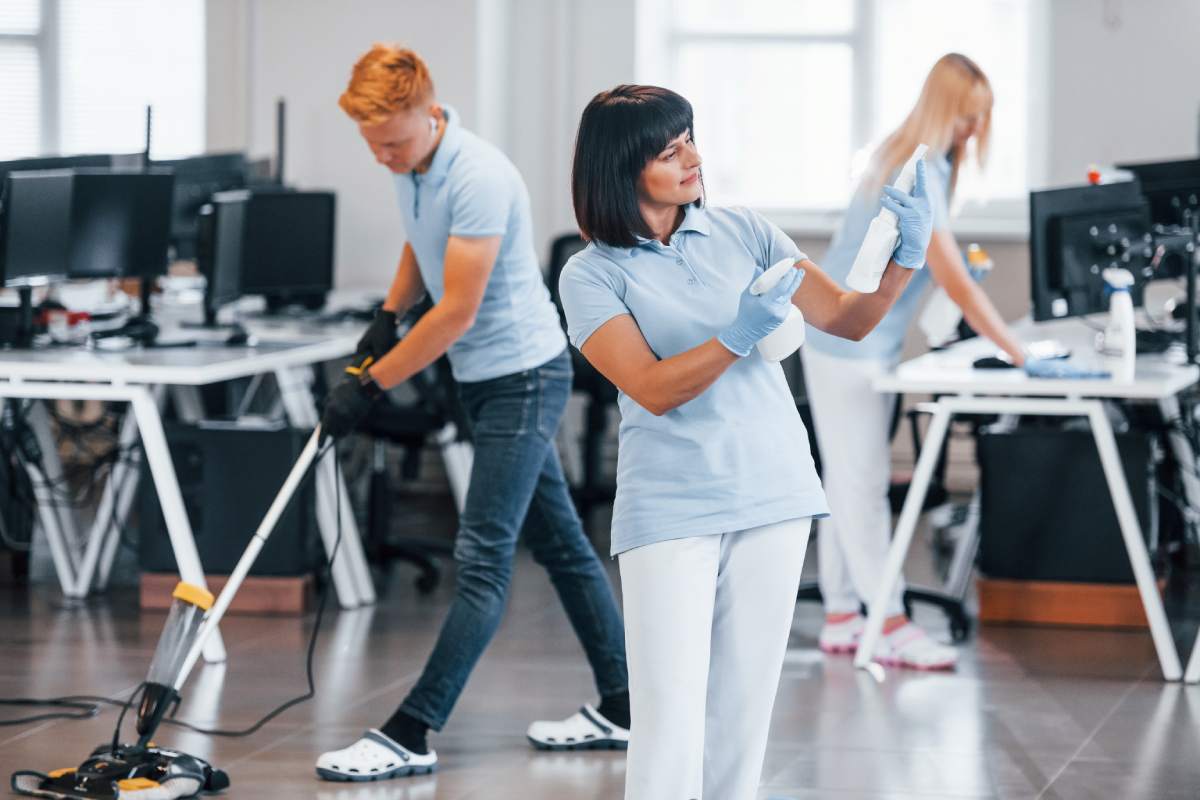 Group of workers clean modern office together at daytime.