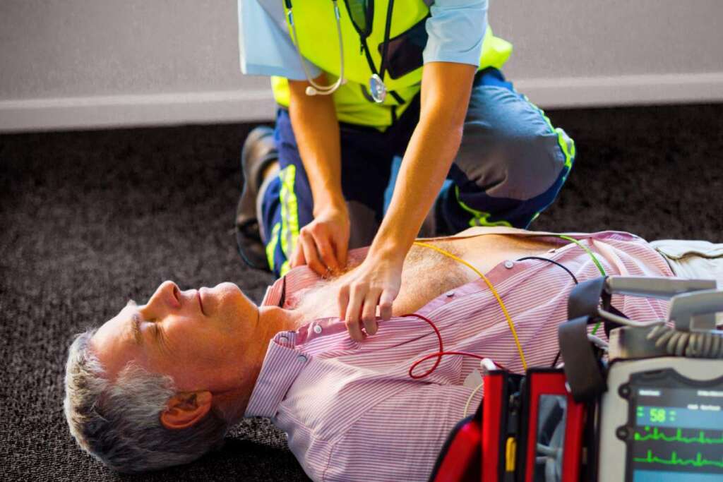 Paramedic using an external defibrillator on an unconscious patient lying on carpet