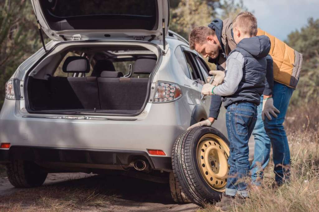 smiling father and son changing car wheel together