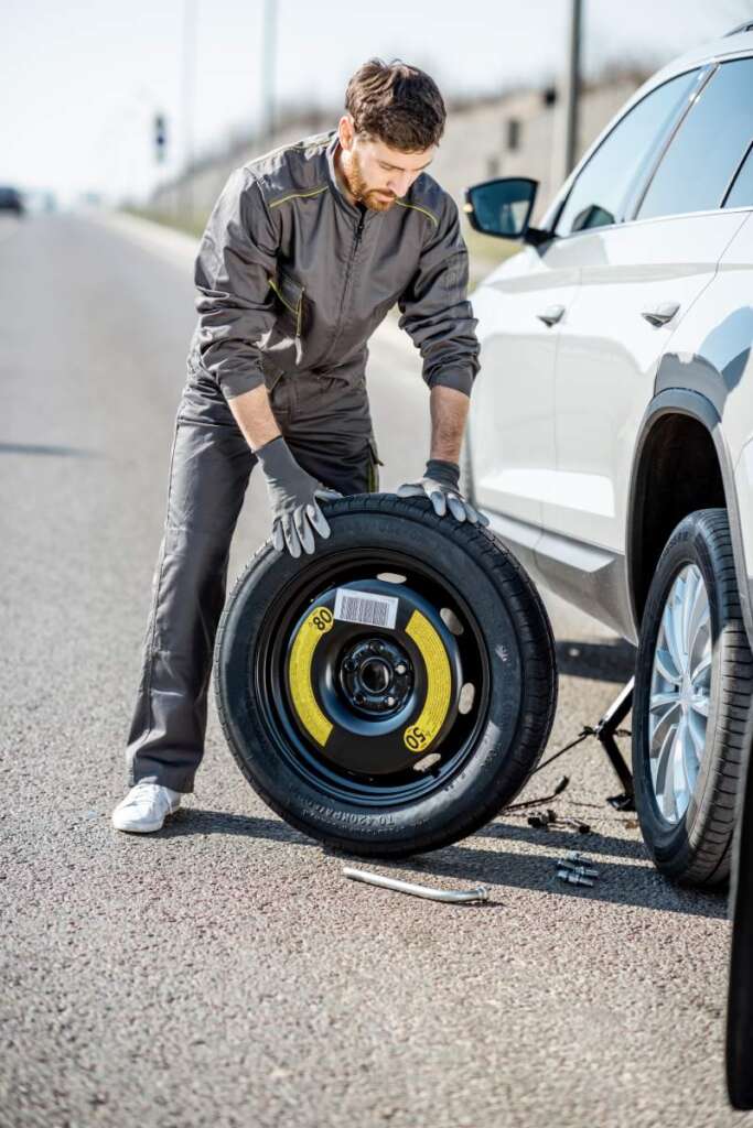 Road assistance worker in uniform changing car wheel on the highway