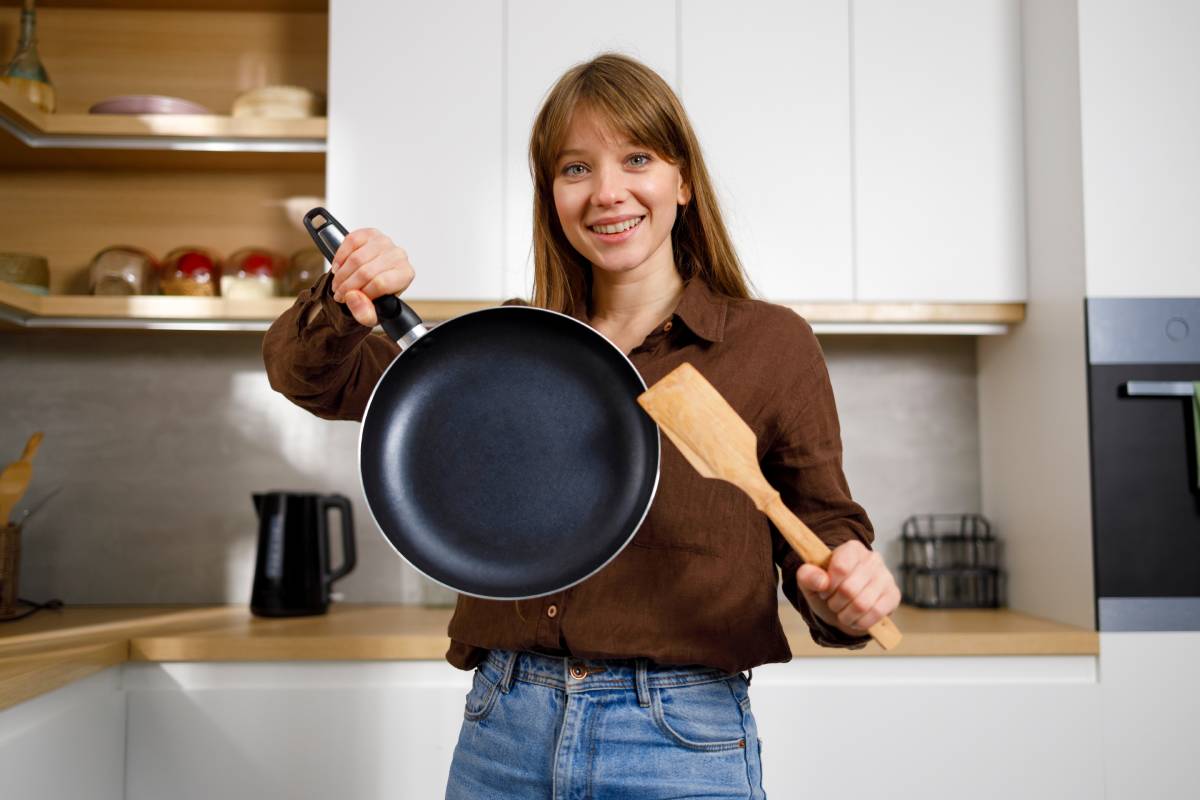 Young housewife with a frying pan and wooden spatula in her hands