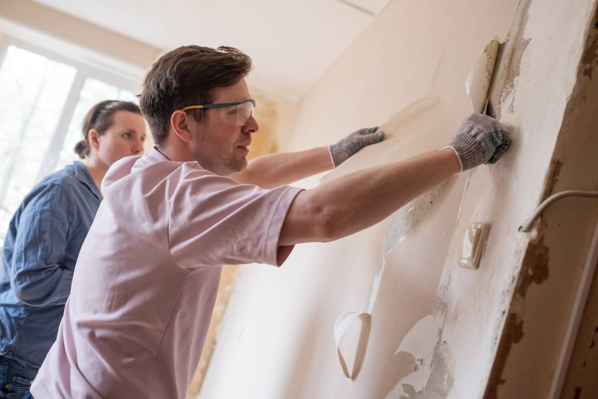 Young caucasian couple removing old wallpaper from walls preparing for flat renovation.